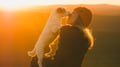 Woman in an orange beanie kisses a small white dog at sunset, both bathed in warm golden light.